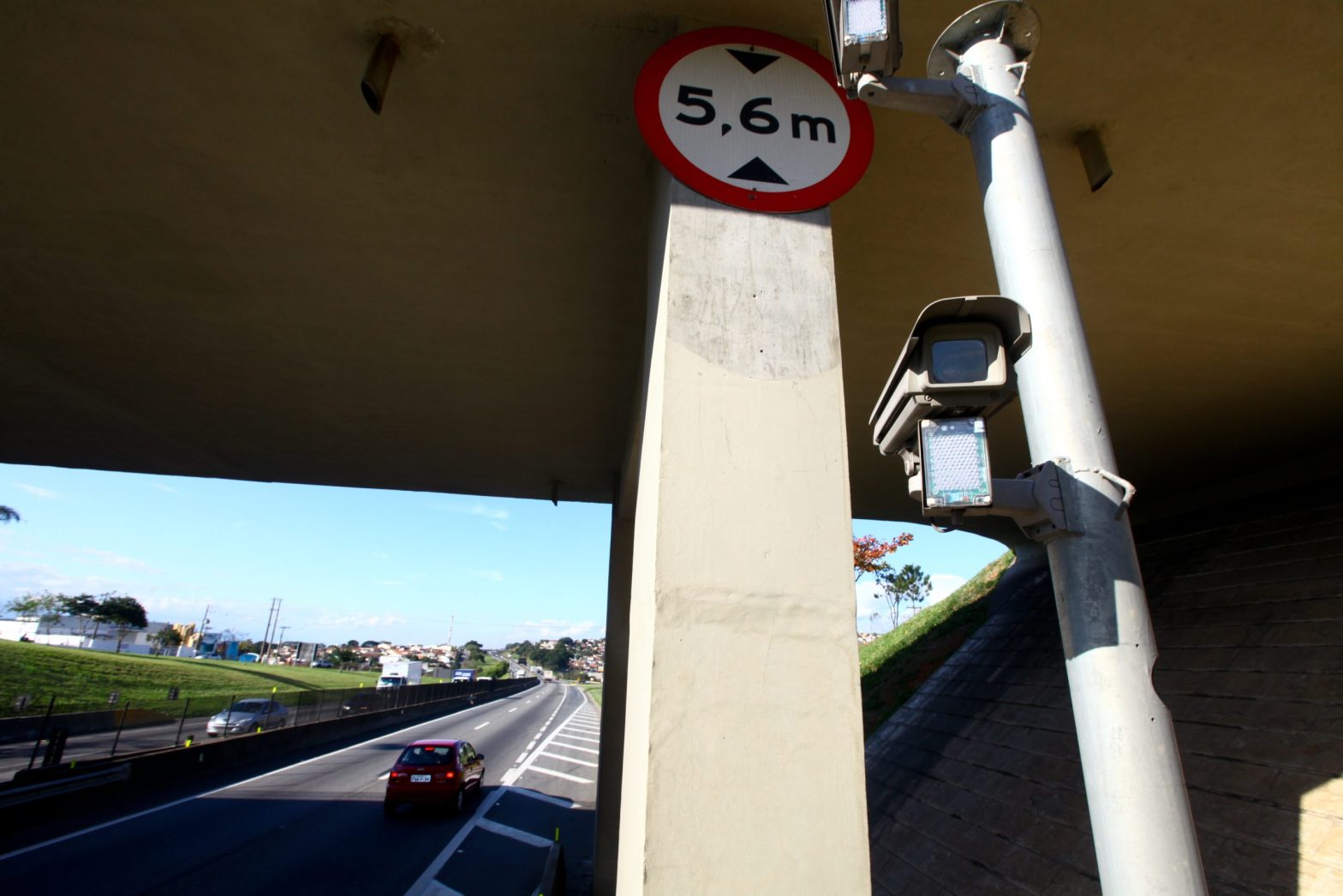 Câmeras rodoviárias instaladas sob viaduto monitorando pista da rodovia, com destaque para sinalização de altura, no contexto de pedágios eletrônicos e Free Flow